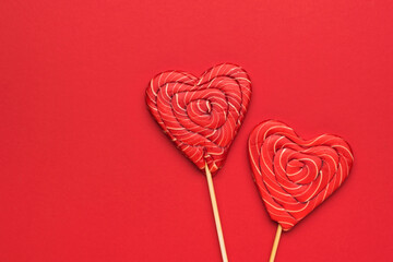 Two large red heart-shaped candies on a stick on a red background. Minimal concept of sweet life and love.