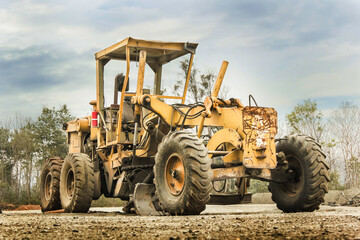 Motor Grader on road construction in forest area. Grader leveling the sand, ground and gravel during road work. Heavy machinery and construction equipment for grading. Earthworks grader machine