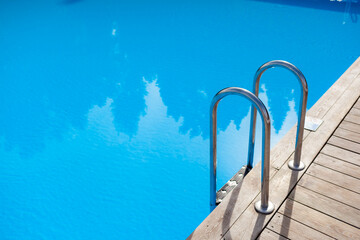 Ladder stainless handrails for descent into swimming pool. Swimming pool with handrail . Ladder of a swimming pool. People swim and relax in the pool