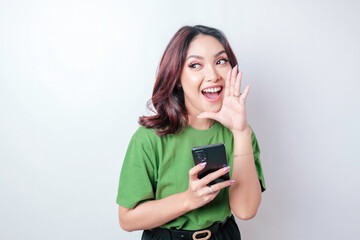 A young Asian woman shouting loud to the side with a hand in her mouth while holding her phone. communication concept.