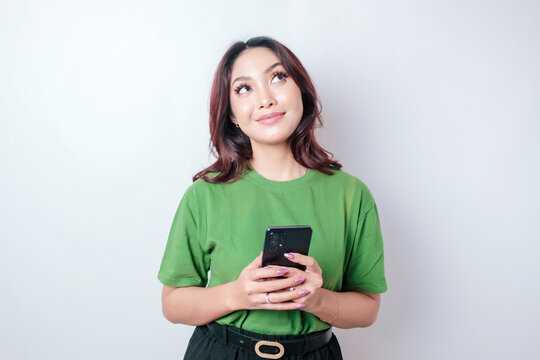 Portrait of a thoughtful young Asian woman wearing green t-shirt looking aside while holding smartphone