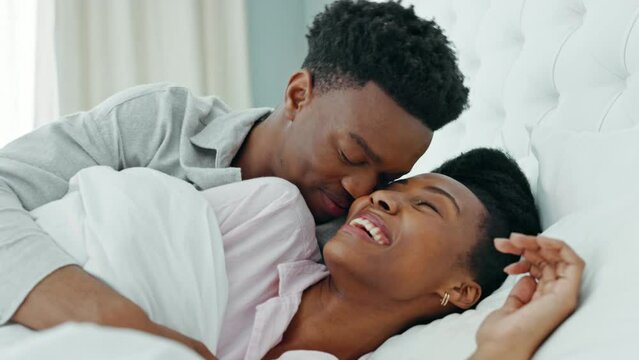 Kissing, morning and couple in bed waking up together in a luxury hotel bedroom or getaway honeymoon retreat. Love, care and happy man, woman or black people cuddle under blankets bonding on weekend