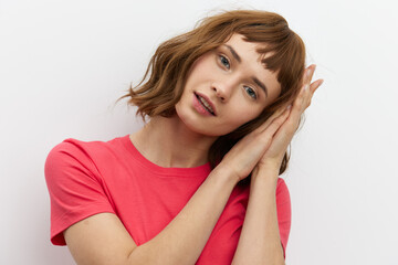 horizontal photo of a cute, attractive, laughing red-haired woman in a red cotton T-shirt standing on a white background and holding her hands near her face.