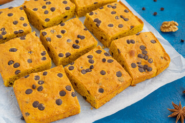 Pumpkin blondie or cake with chocolate drops, walnuts, cinnamon and anise on baking paper on a blue concrete background. Dessert for Thanksgiving or Halloween.