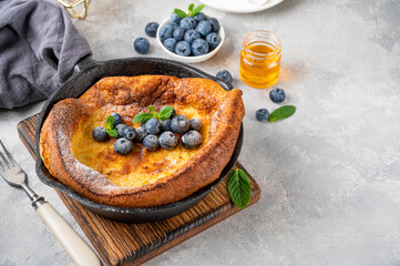 Homemade Dutch Baby pancake with fresh blueberries, mint and sprinkled with icing sugar in iron skillets on a gray concrete background. Copy space.