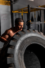 Fototapeta na wymiar High quality photo. A Latino man in the gym pushing a very large tire. A shirtless Hispanic man doing cardio and strength training with a giant tire.