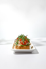 Aesthetic composition with shrimp bruschetta on white background with shadows from flowers. Italian bruschetta with shrimp, tomatoes and arugula on fine dining in summer. Elegant menu concept.