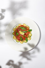 Beef carpaccio with zucchini and cucumber on white table with sunlight shadows. Appetizer of meat - beef carpaccio on summer dining. Sliced raw meat in italian style. Aesthetic menu.