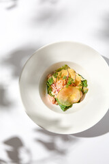 Elegant salad with crab meat, espuma sauce and lettuce on white table with harsh shadows. Green salad with crab and creamy sauce in summer menu. Aesthetic food. Seafood appetizer.