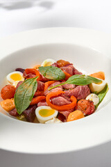 Salad with roast beef, vegetables and eggs on white table with harsh shadows. Steak salad in modern style with shadows of leaves. Flashy food. Meat salad with pastrami in summer menu.