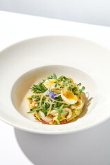 Healthy salad with squid and avocado on white plate with harsh shadows. Calamari salad with vegetables and eggs on white background with shadows of leaves. Summer food menu.