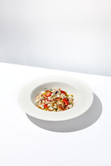 Elegant salad with smoked eel, strawberry and avocado on white table with harsh shadows. Eel salad with berries on white background with shadows of leaves. Romantic dining with fish appetizer.