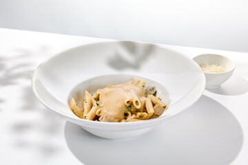 Italian pasta penne with chicken and mushrooms in creamy sauce. Mushroom and chicken pasta on white plate with shadows of sunlight. Summer italian lunch Penne with mushroom sauce on light background