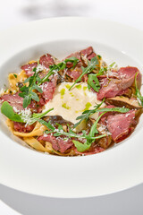 Homemade pasta with pastrami and creamy sauce with cheese. Italian pasta pappardelle with beef and sauce on white table Italian food in summer dining with shadows of sunlight