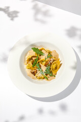 Italian ravioli with meat and mushroom sauce on white plate. Meat tortellini with creamy sauce in summer menu with shadows of tree leaves Ravioli stuffed beef in elegant style