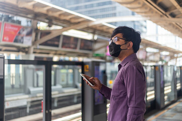 Young asian man using smartphone while waiting for sky train.