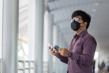 asian man with surgical face mask using creadit card and smartphone. City on day background with copy space.