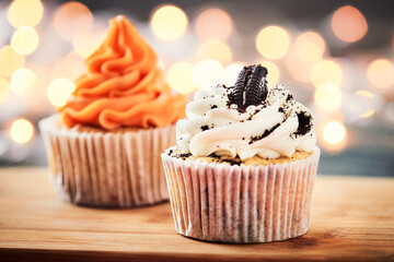 Two cupcakes decorated with orange and chocolate cookie cream and festive lights on the background.