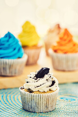 Four cupcakes decorated with colorful and chocolate cookie cream on a table.