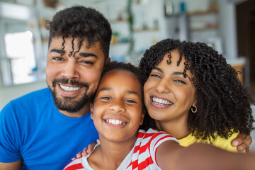 Fototapeta premium Happy african family with daughter having fun with gadget on couch using smartphone at home, parents and kid make video call selfie on phone online app