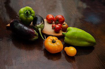 tomatoes,  peppers and eggplants scattered on a cutting board and on the table, fresh vegetables