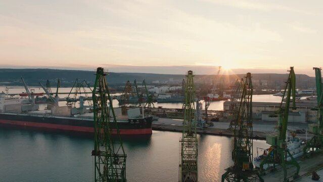 Aerial view loading of dry cargo ship of wheat by cranes in port for import of transportation on water against sunset. Export and import of dry cargoes world. Large cargo compartments in hold of ship