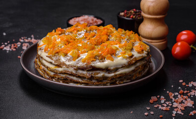 Delicious fresh liver cake with mayonnaise and carrots on a black plate against a dark concrete background