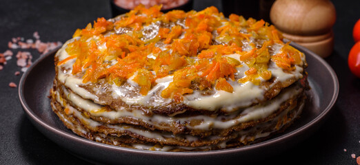 Delicious fresh liver cake with mayonnaise and carrots on a black plate against a dark concrete background