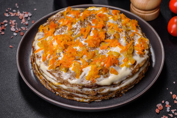 Delicious fresh liver cake with mayonnaise and carrots on a black plate against a dark concrete background