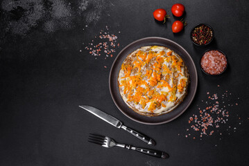 Delicious fresh liver cake with mayonnaise and carrots on a black plate against a dark concrete background