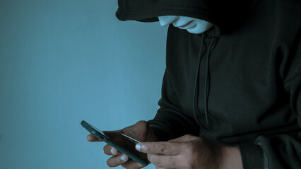 An anonymous masked hacker is using a smartphone to penetrate credit card financial information....