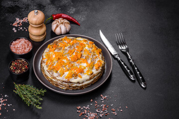 Delicious fresh liver cake with mayonnaise and carrots on a black plate against a dark concrete background