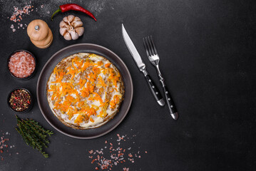 Delicious fresh liver cake with mayonnaise and carrots on a black plate against a dark concrete background