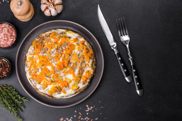 Delicious fresh liver cake with mayonnaise and carrots on a black plate against a dark concrete background