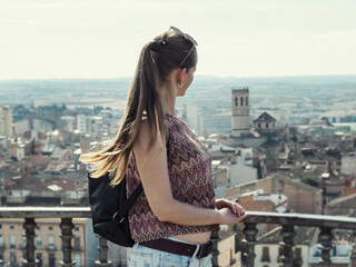 Adult tourist girl with long blonde hair looks at Tarrega city (Catalonia, Spain) from the observation deck. Woman close-up on the background of a panorama of the Spanish town with an old tower