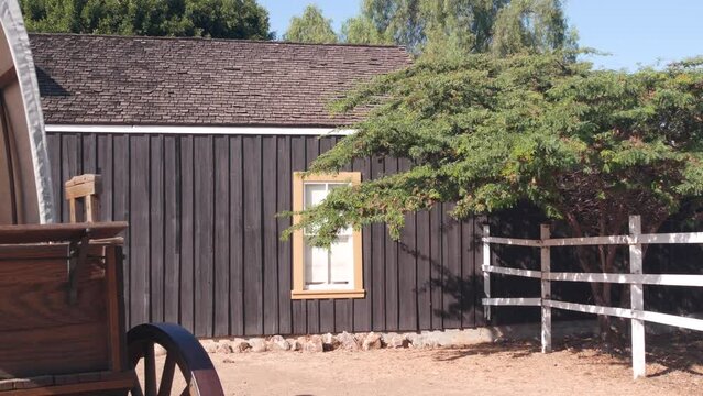 Old wooden retro covered wagon on wheels, wild west pioneer ranch. Western historic retro cart, traditional vintage transport. Rural house wall, building exterior. Countryside farm or cowboy saloon.