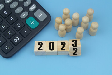 Numbers 2023 and 2022 on wooden cubes, calculator and people figures on blue background. Financial prognosis and analytics for year 2023 and 2022.