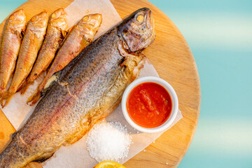 Large and small fried fish on a wooden board, Sauce, salt. close-up.