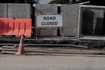 Under construction street with ROAD CLOSED word shown on white traffic signboard and group of concrete drainage tunnel block as barrior. Rough and grain textured of cement wall on uncompleted roadway.