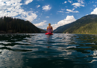 Adventurous athletic woman sitting on a paddle board on a large alpine lake in the Pacific Northwest on a beautiful summer day.
