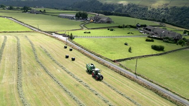 Green Tractor harvesting hay on a rural English landscape aerial view. Nature scenery. Farming scene