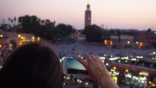 4K Footage of a woman takig pictures with her smartphone on a rooftop at djemaa el-Fnaa market durign sunset