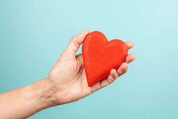 Obraz premium Woman hand holding red wooden heart on light blue background. Love, care, donation concept