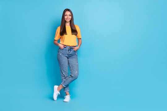 Full size photo of young cute nice woman long hairstyle wear yellow t-shirt arms in pockets legs crossed isolated on blue color background