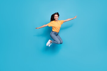 Obraz premium Full length photo of adorable pretty girl dressed yellow t-shirt arms sides jumping high isolated blue color background