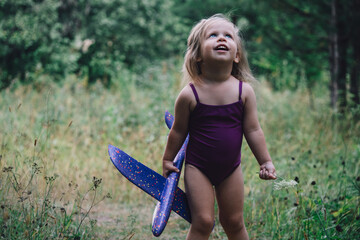 A little girl in a swimsuit lifted the plane and looks joyfully, admiringly and dreamily into the sky. Traveling with a child concept. Children's imagination: become a pilot, fly an airplane