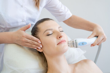 Obraz na płótnie Canvas Handle radio frequency apparatus on chin woman's face during skin rejuvenation beauty lifting procedure. The beautician makes the hardware face of a woman of a cute woman.
