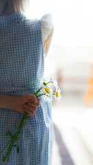 A little girl holding a bouquet of daisies behind her back
