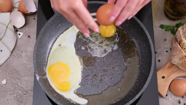 Woman breaks egg into hot frying pan on stove
