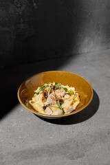 Italian pasta Pappardelle with chicken and mushrooms in creamy sauce on gray stone table Creamy pasta pappardelle with chicken meat and mushroom Fettucine with fungi on concrete background with shadow